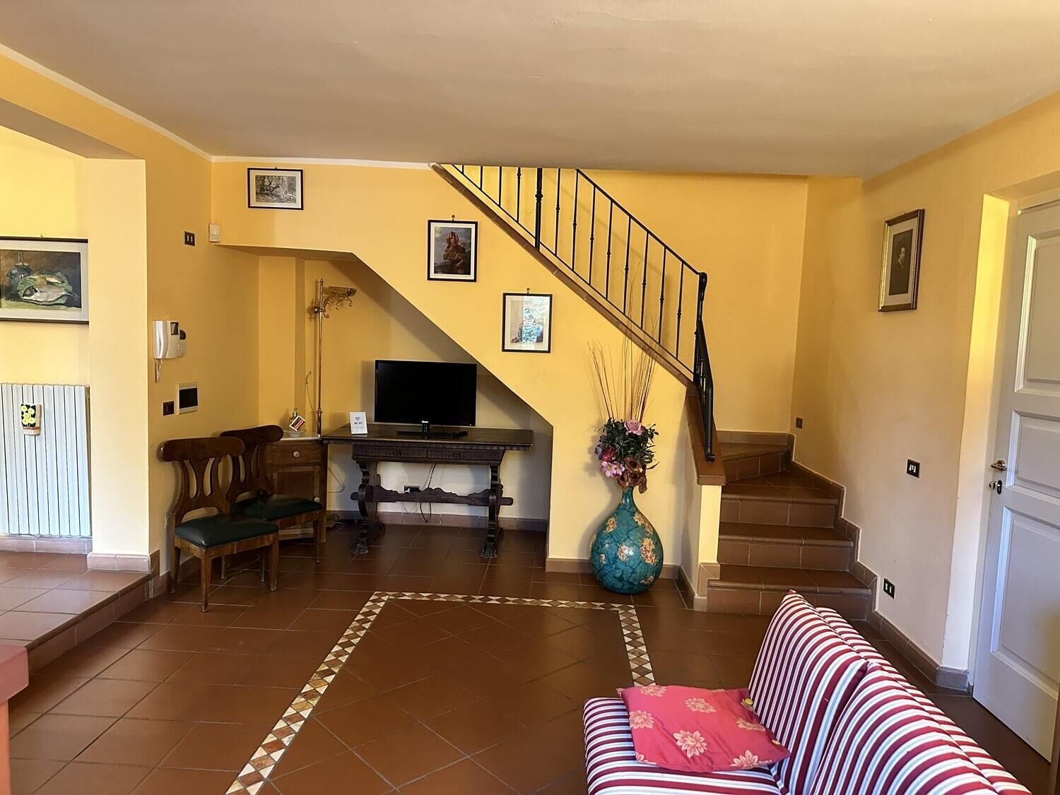 A living room with a sofa, a television, a staircase, and a decorative vase.