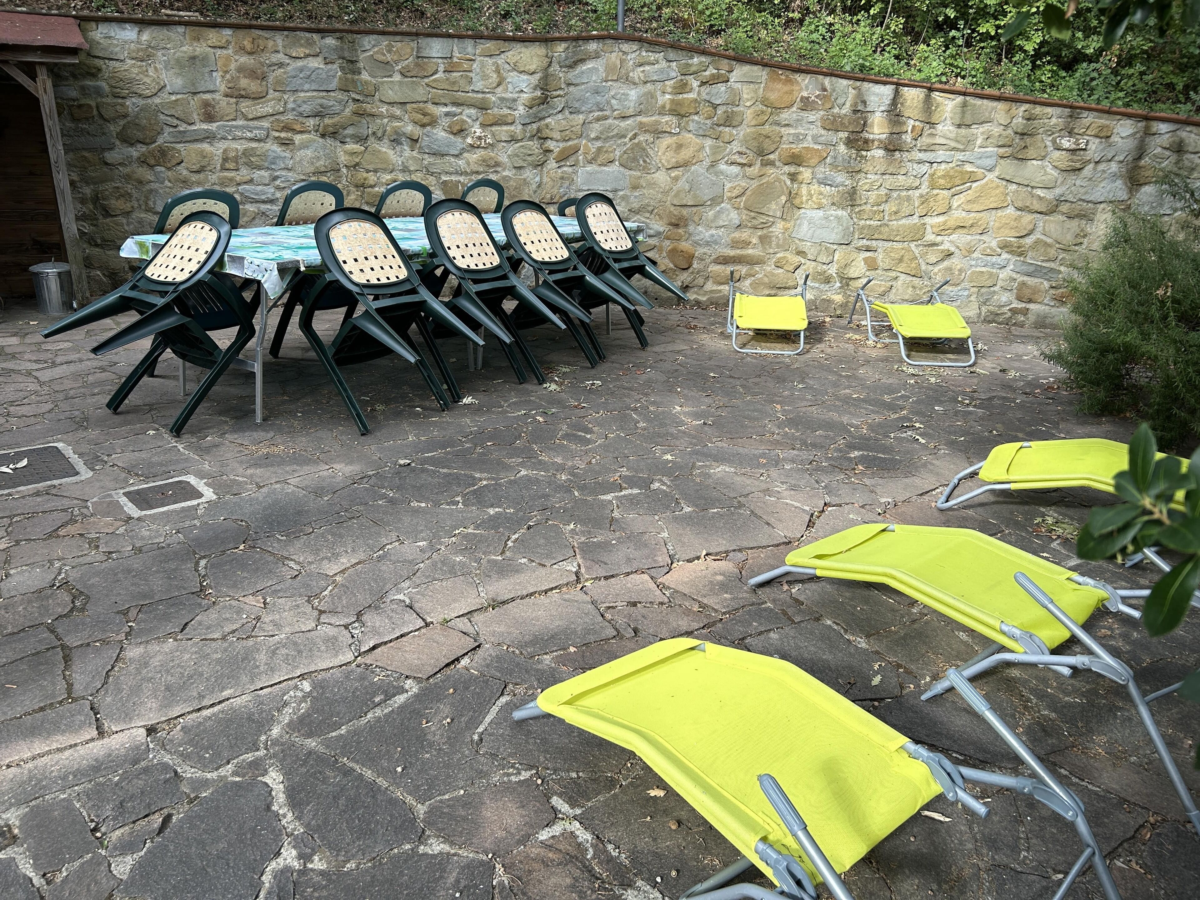 A stone patio with outdoor seating, including green and yellow chairs, and a stone wall in the background.