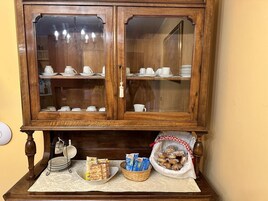 Un aparador de madera con puertas de cristal que contiene vajilla blanca y una mesa debajo con alimentos y una cesta.