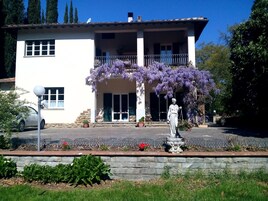 Un edificio de dos pisos con un balcón, una estatua y enredaderas moradas con flores.
