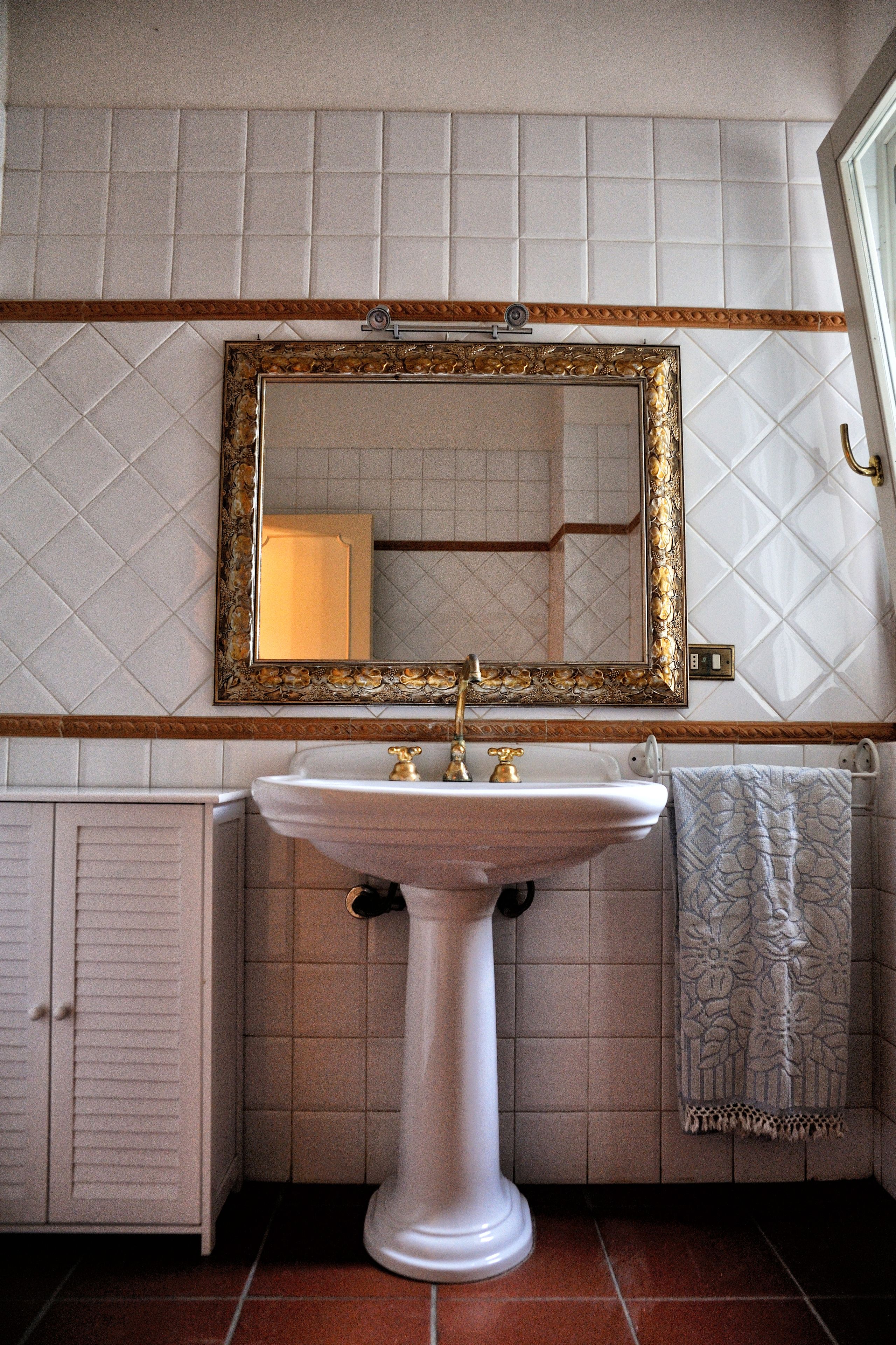 A bathroom with a pedestal sink, a large mirror with an ornate frame, and a towel hanging on a rack.