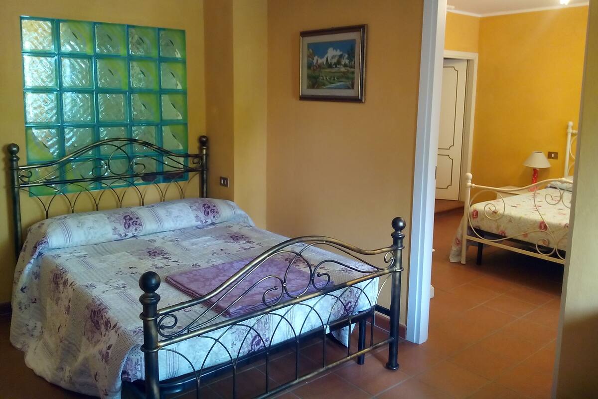 A bedroom with a bed, a window with green glass, a door, and a painting on the wall.