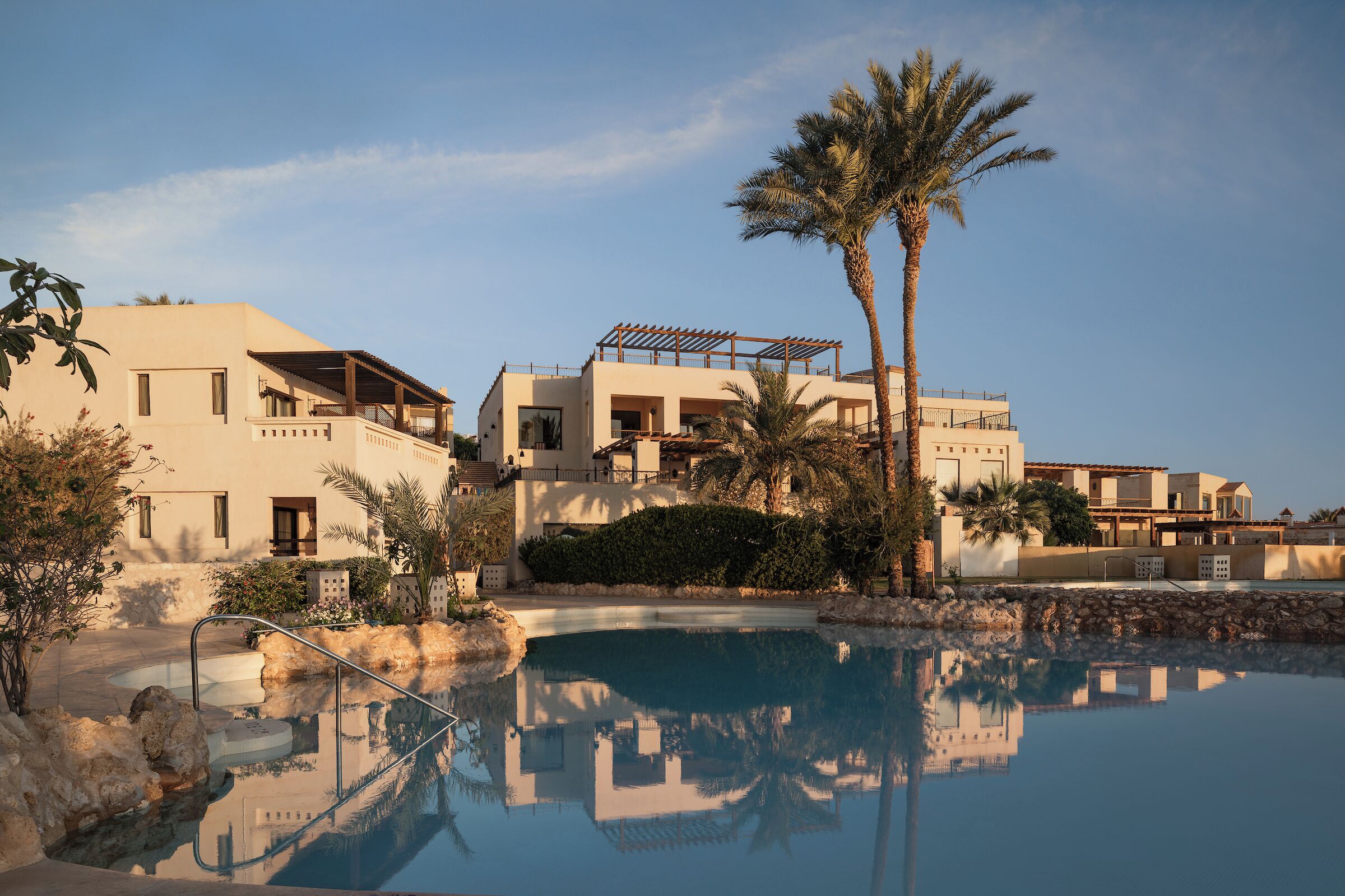 Ein Resort mit Swimmingpool, Palmen und modernen Gebäuden.