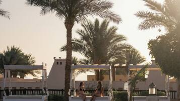 A pool area with palm trees and a person sitting on a bench.