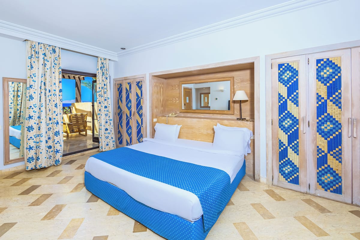 Une chambre d’hôtel avec un grand lit, une tête de lit en bois, un miroir et une armoire aux portes à motifs.