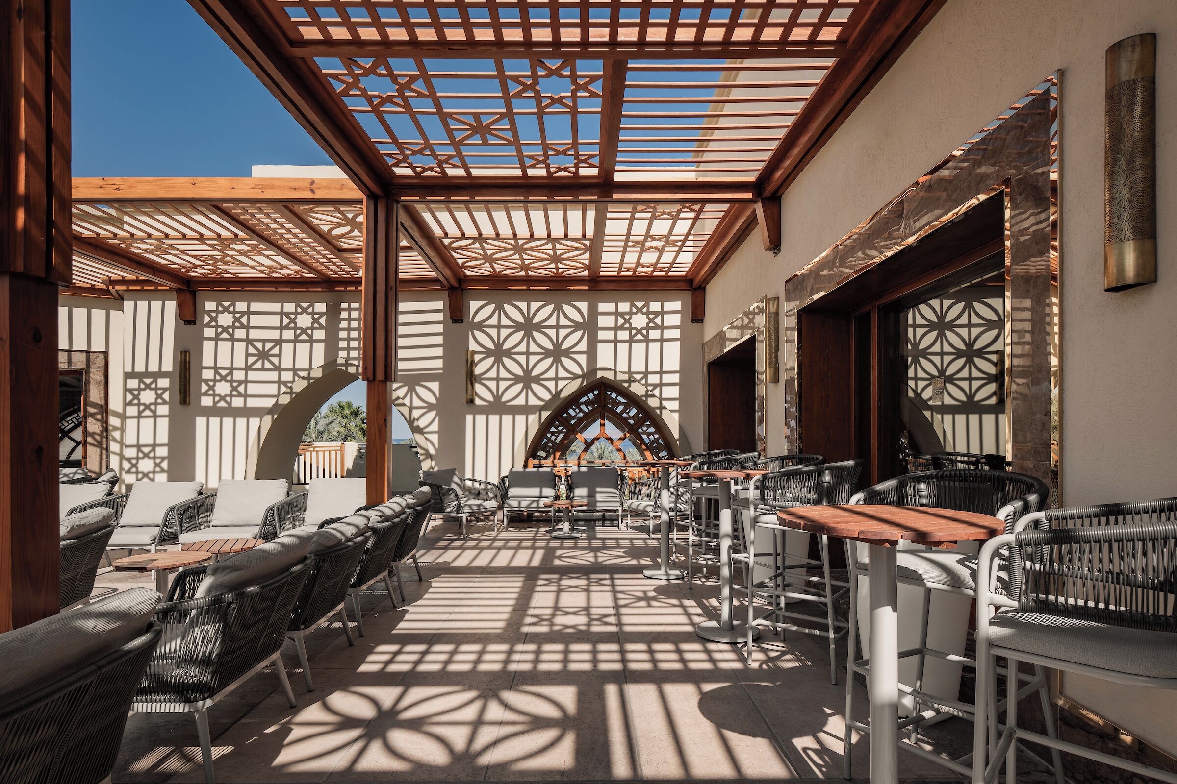 Un espacio de estar al aire libre con mobiliario de mimbre, una mesa de madera y una estructura decorativa en el techo.