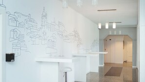 A modern hotel lobby with a minimalist design, featuring a long reception desk, a bar area, and a wall with architectural line drawings. - Hotel Voar (Ribadeo)
