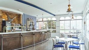 A modern bar area with a stone accent wall, a counter with a vintage espresso machine, and a seating area with white tables and blue chairs. - Hotel Voar (Ribadeo)