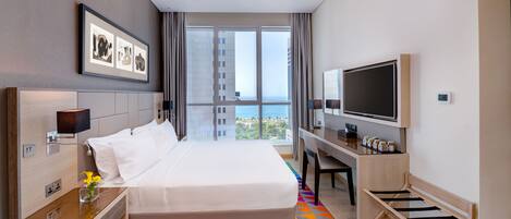 Habitación de hotel con una cama grande, un escritorio con televisor y vistas a la ciudad.
