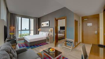 Une chambre d’hôtel avec un grand lit, un canapé, une petite table avec des fruits, une télévision et une vue sur l’extérieur.