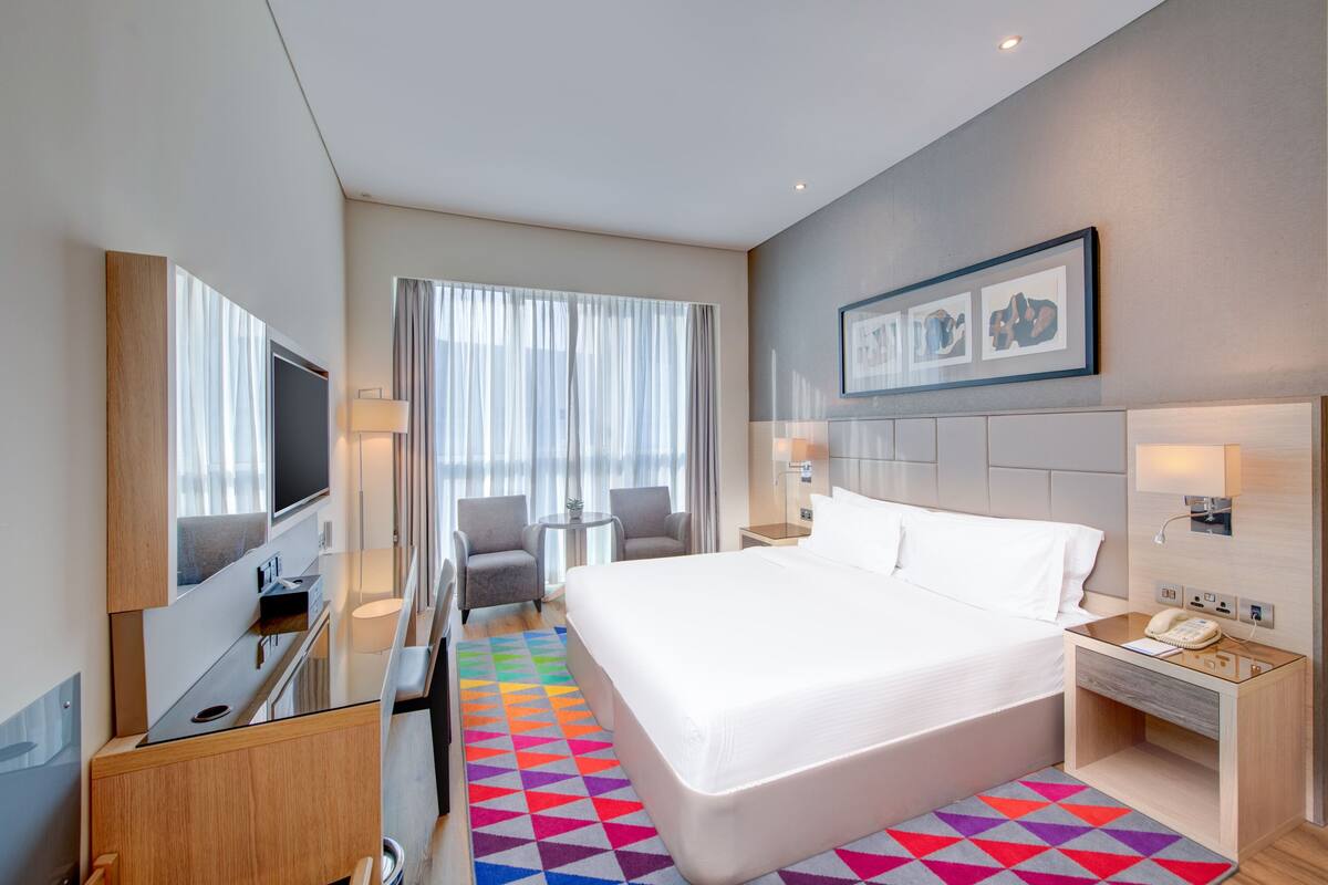 A modern hotel room with a large bed, a TV, a desk, and a chair.
