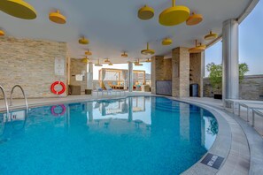A swimming pool with clear blue water, surrounded by stone walls and yellow ceiling lights. - TRYP by Wyndham Abu Dhabi City Centre (Abu Dhabi)