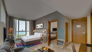 Een hotelkamer met een groot bed, een bank, een klein tafeltje met fruit, een televisie en uitzicht op het groen.
