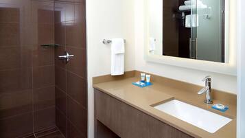 A modern bathroom with a glass shower enclosure, a beige vanity with a sink, and a large mirror above the vanity.