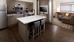 Een moderne keuken met een centraal eiland, barkrukken, een flatscreen televisie en een zithoek met een bank en een lamp.