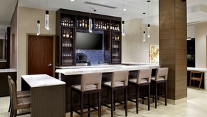 Een moderne bar met een flatscreen televisie, barstoelen en kasten vol flessen en glazen.
