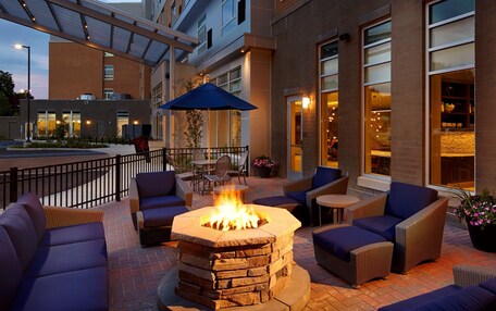 An outdoor seating area with a stone fire pit, cushioned sofas, and a table with chairs.