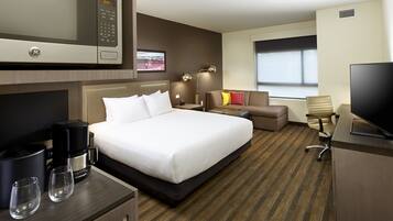 Habitación de hotel con cama, escritorio con computadora, microondas, cafetera y televisor.