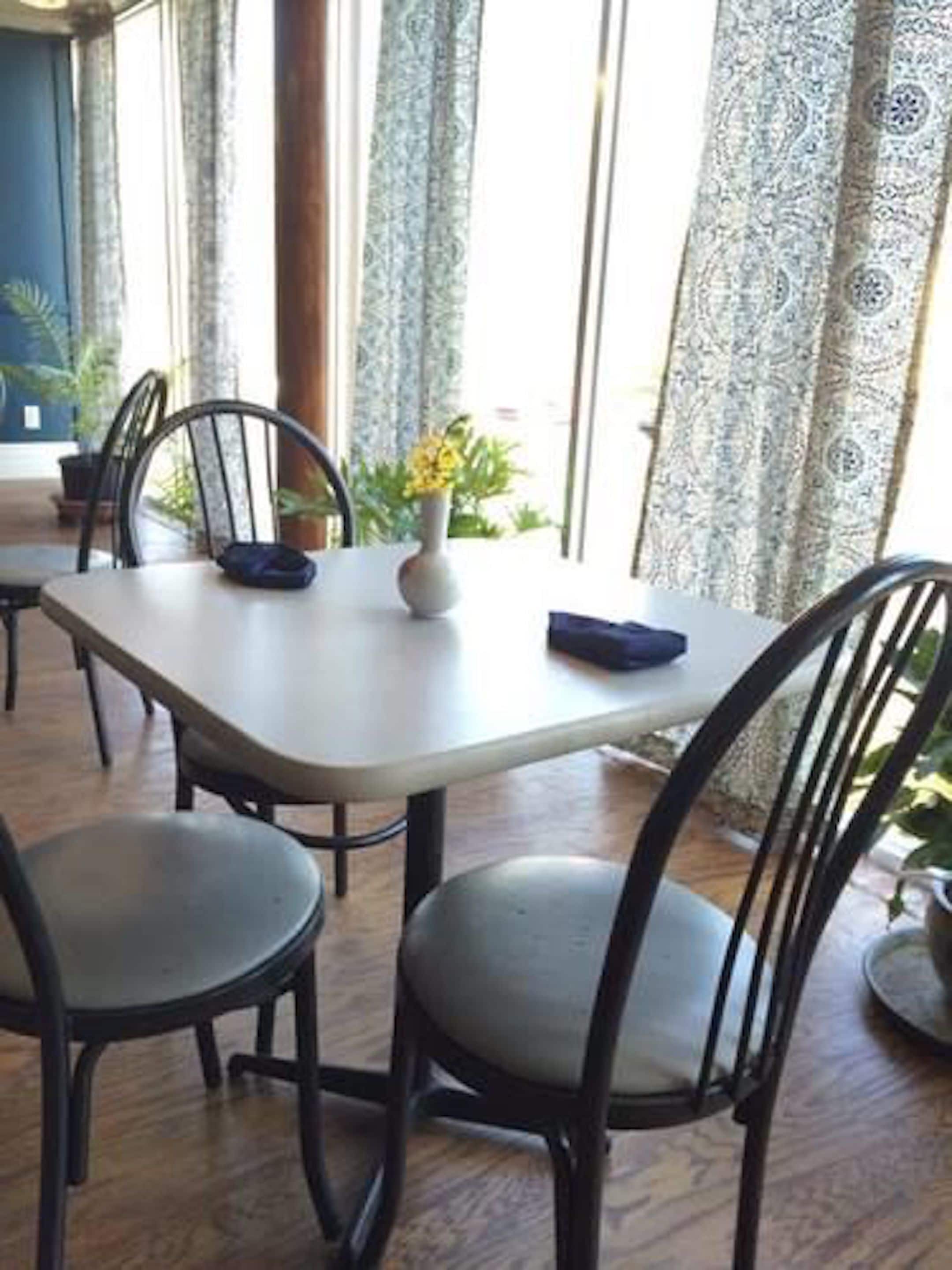 Un coin repas avec une table et des chaises, un vase rempli de fleurs et une vue dégagée grâce à de grandes fenêtres.