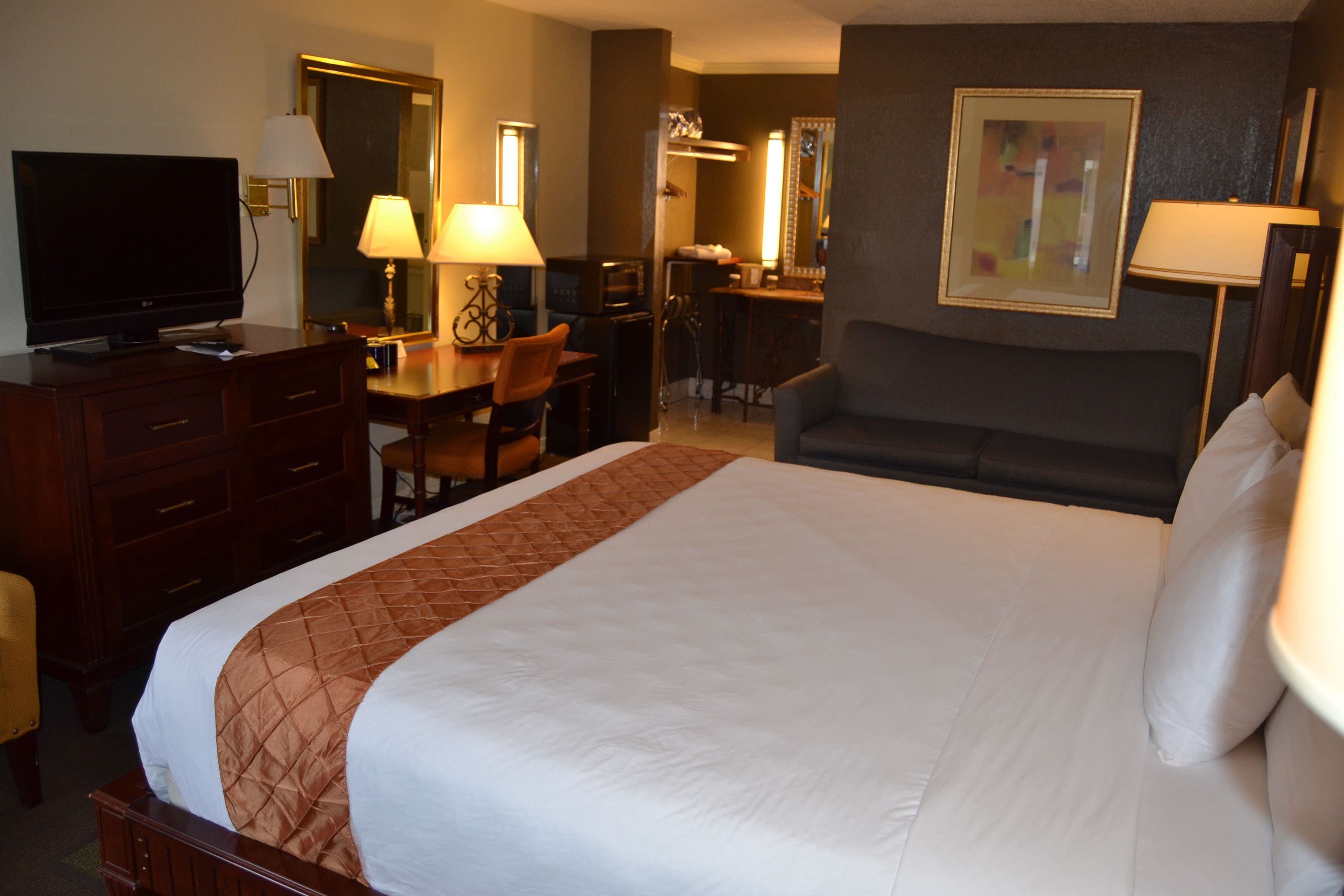 Habitación de hotel con una cama grande, televisión, escritorio con silla, sofá y espejo.