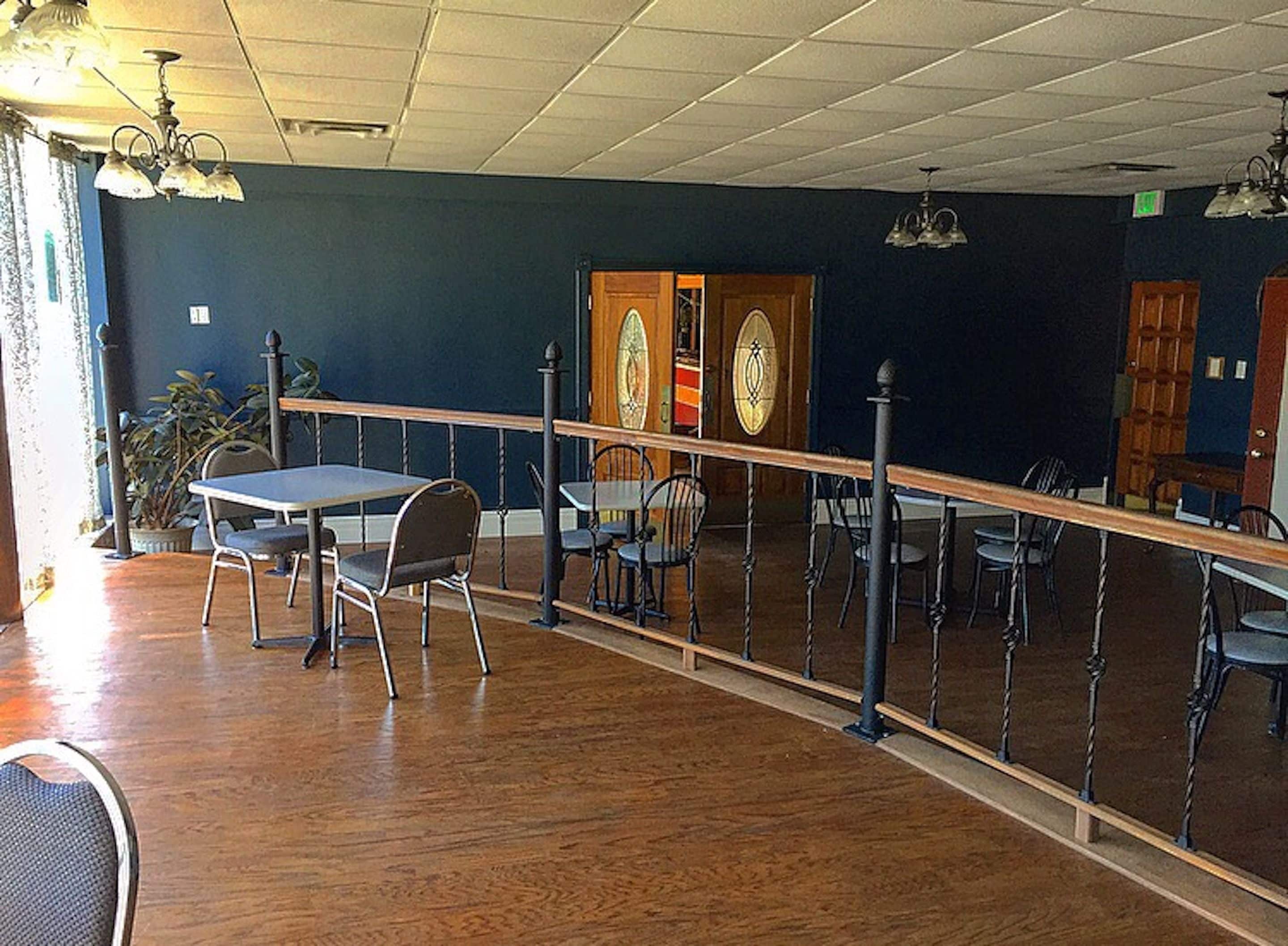 A dining area with tables and chairs, wooden flooring, and a railing.