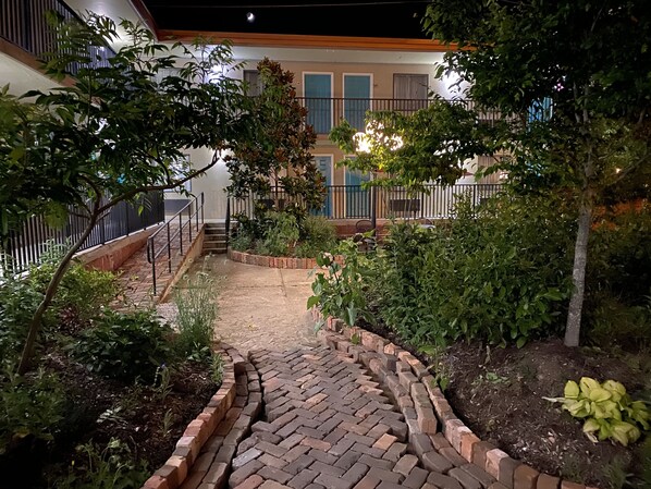 Stroll along the brick pathway to the stairs, surrounded by lush greenery and a secure metal railing.