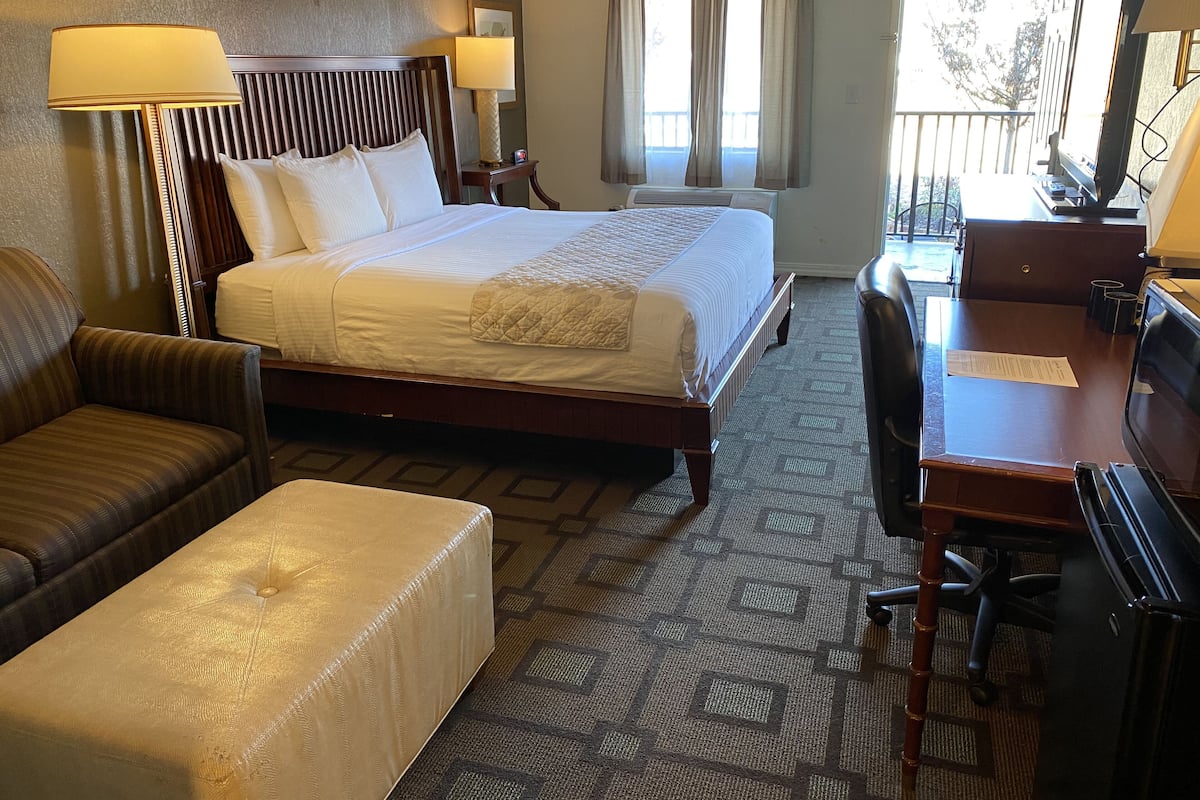 A hotel room with a bed, a desk, a chair, a sofa, and a window with curtains.