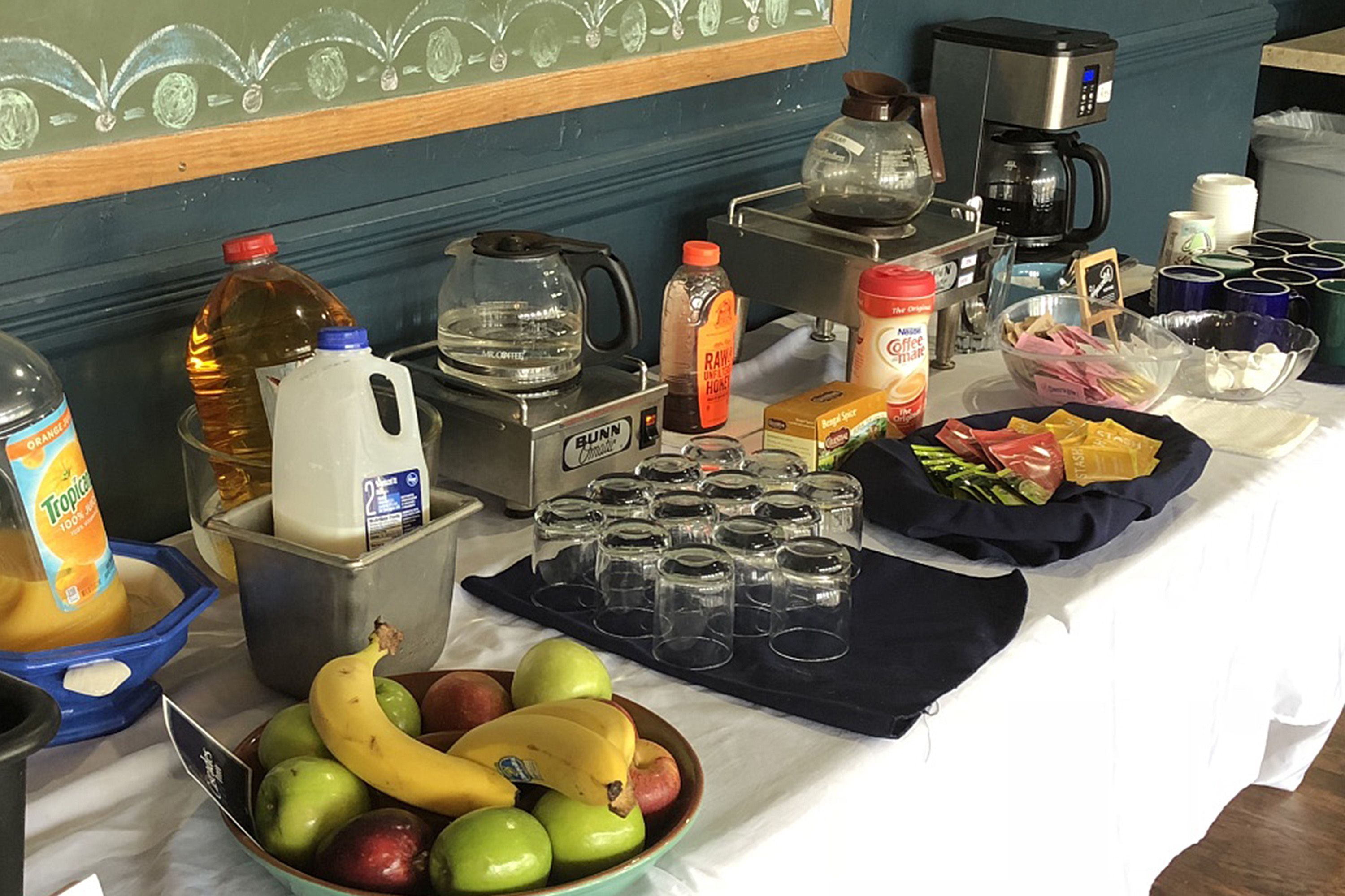 A table with various food items, a coffee maker, and a Bunn coffee grinder.