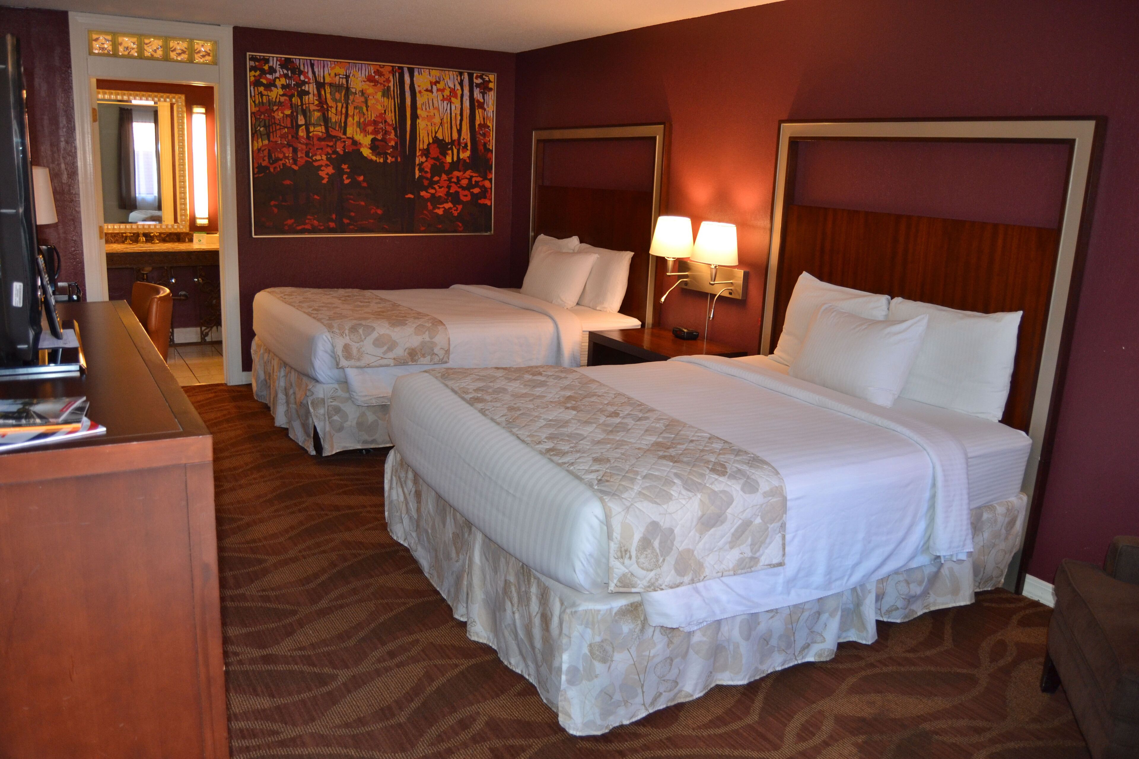Une chambre d’hôtel avec deux lits, un bureau, une chaise, un miroir et un tableau au mur.