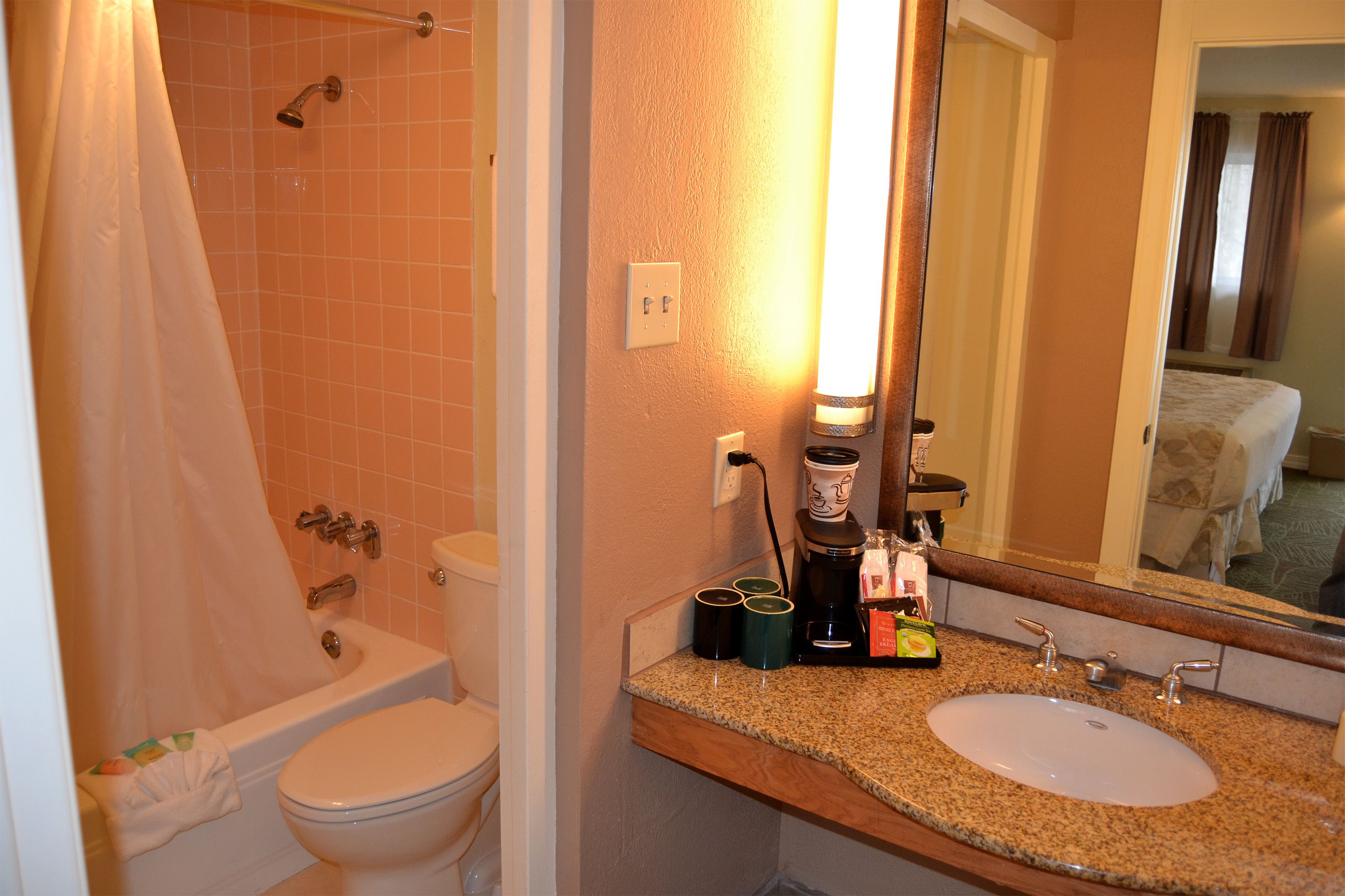 A bathroom with a sink, toilet, and shower. There are cups and a coffee maker on the counter.