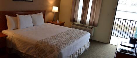 A hotel room with a large bed, a nightstand, a lamp, a window with curtains, and a view of the outside.