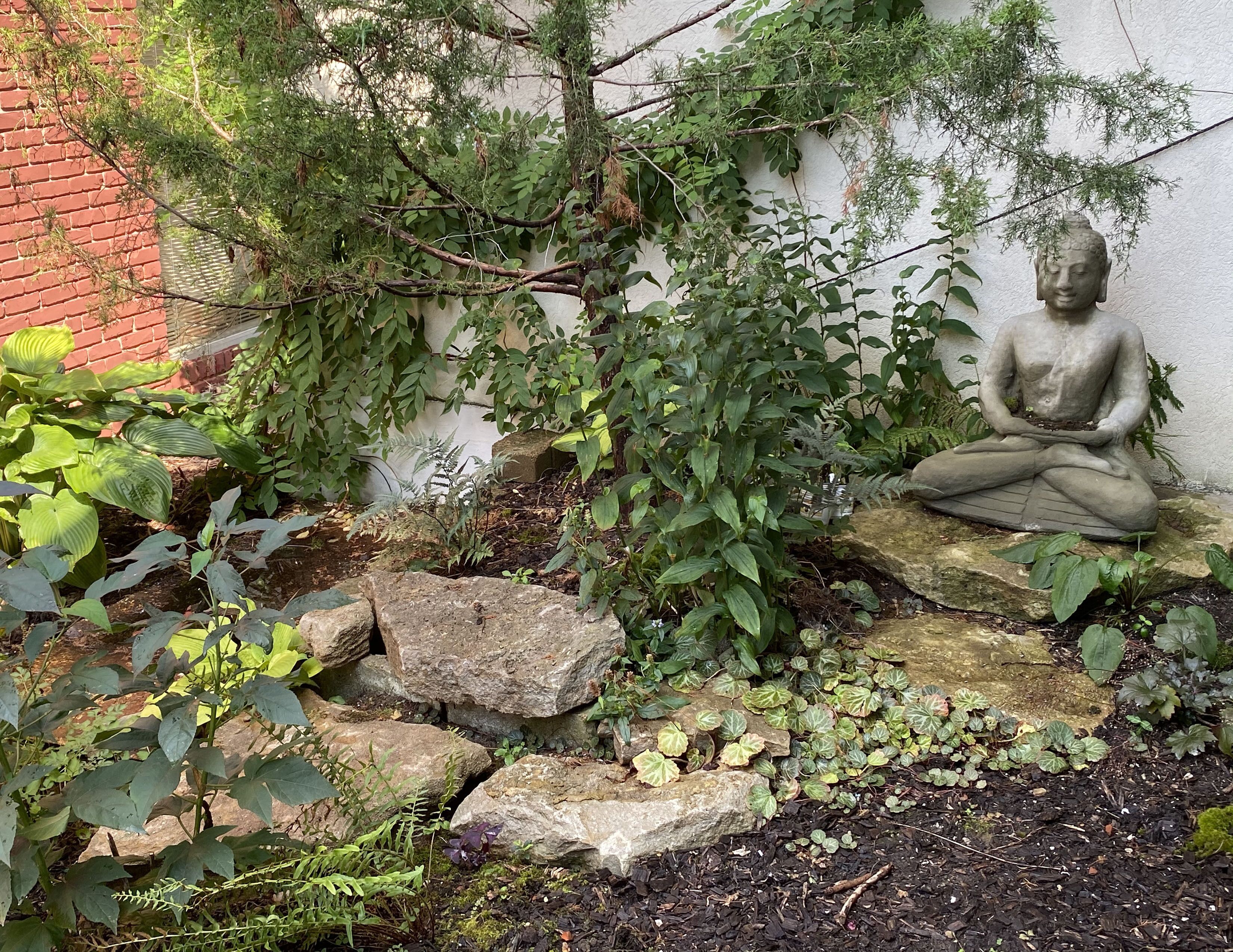 A garden with a Buddha statue, rocks, and various plants.