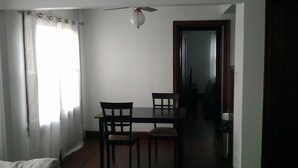 Un comedor con una mesa y sillas, un ventilador de techo y vista a otra habitación.