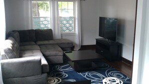 Una sala de estar con un sofá modular, un televisor de pantalla plana, una mesa de centro y un tapete estampado.