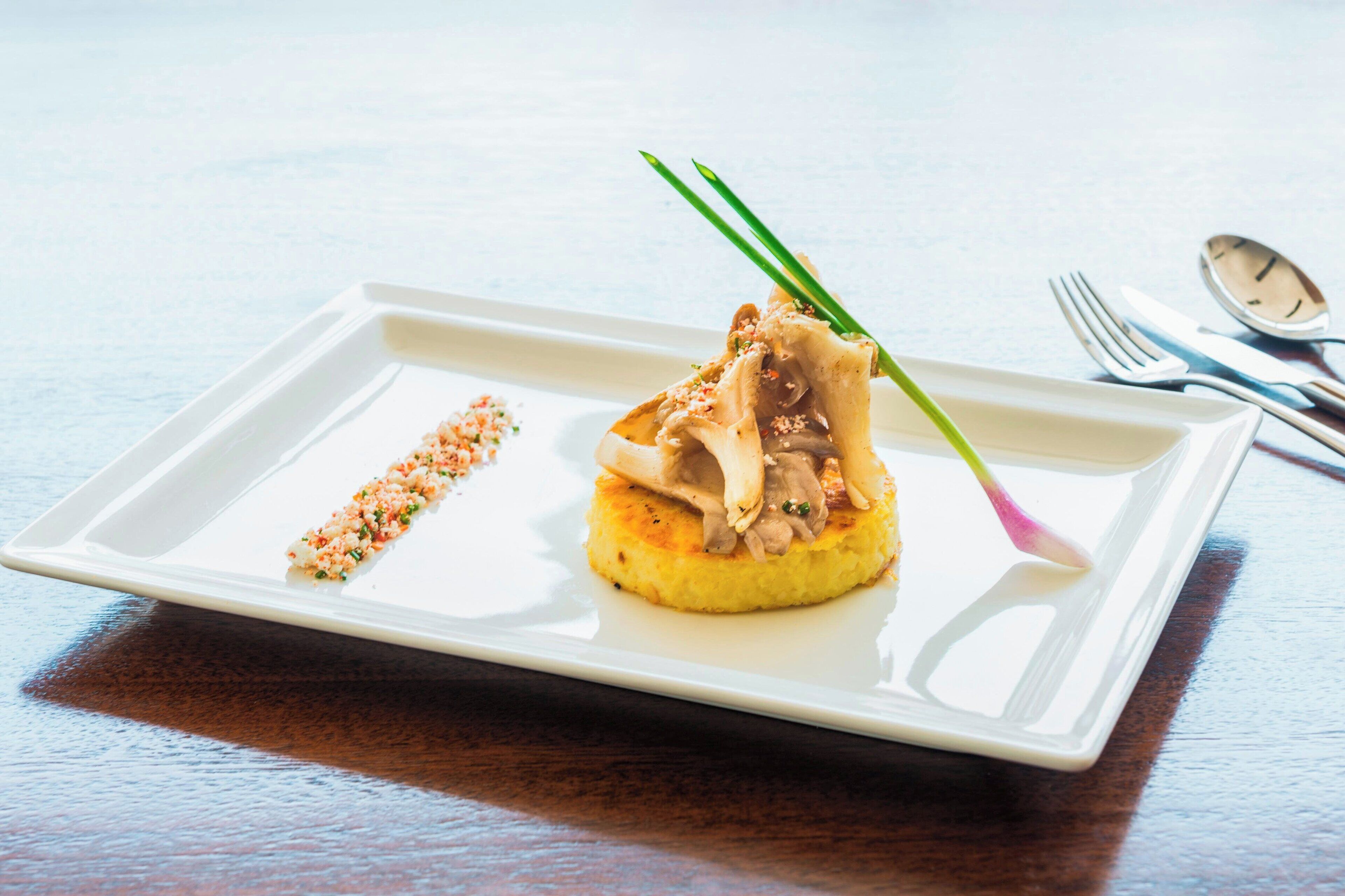 Un plato rectangular blanco con base amarilla, coronado con un bocado de comida y decorado con cebollines verdes.