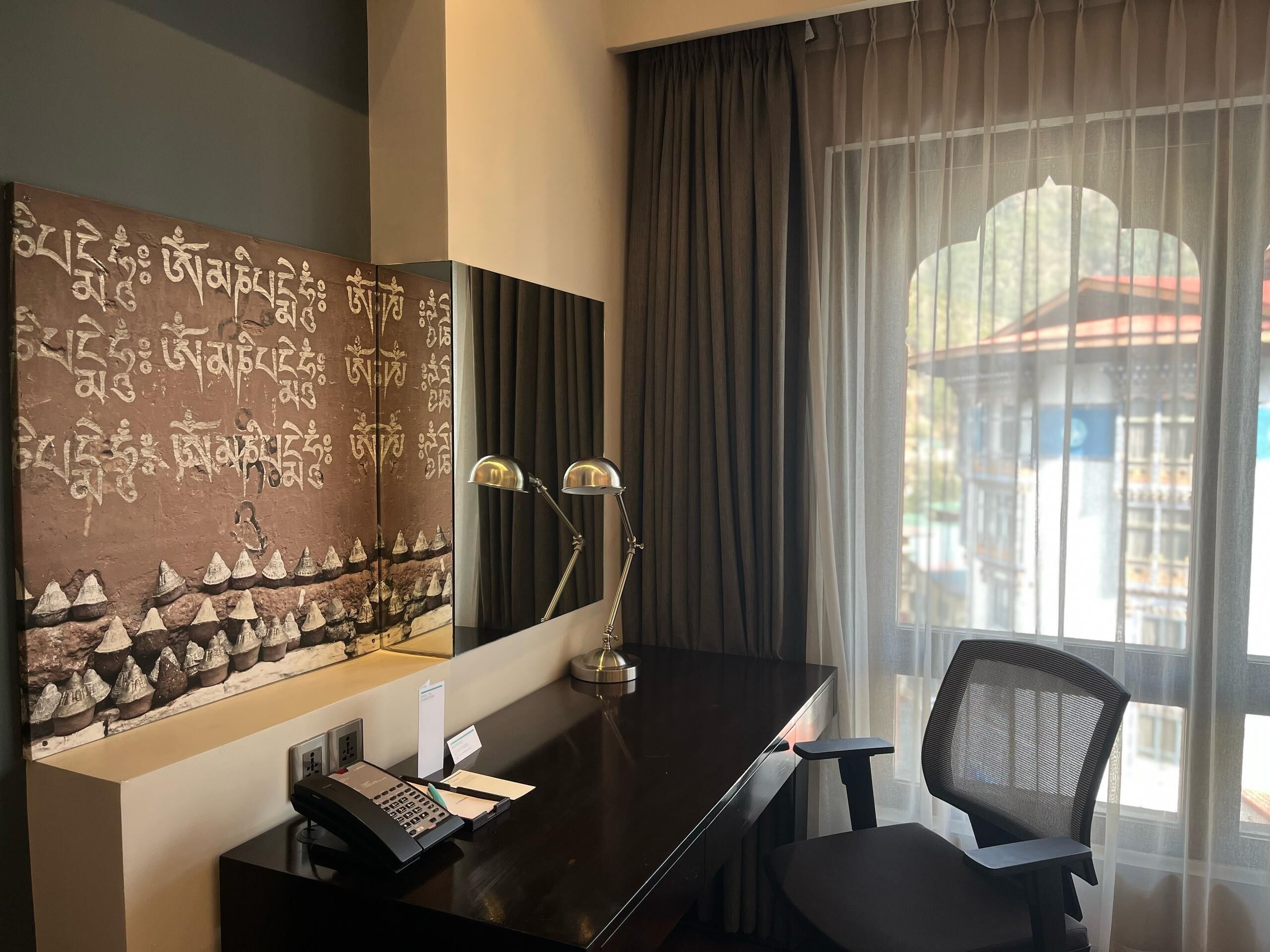 A hotel room with a desk, chair, and a large window with curtains.