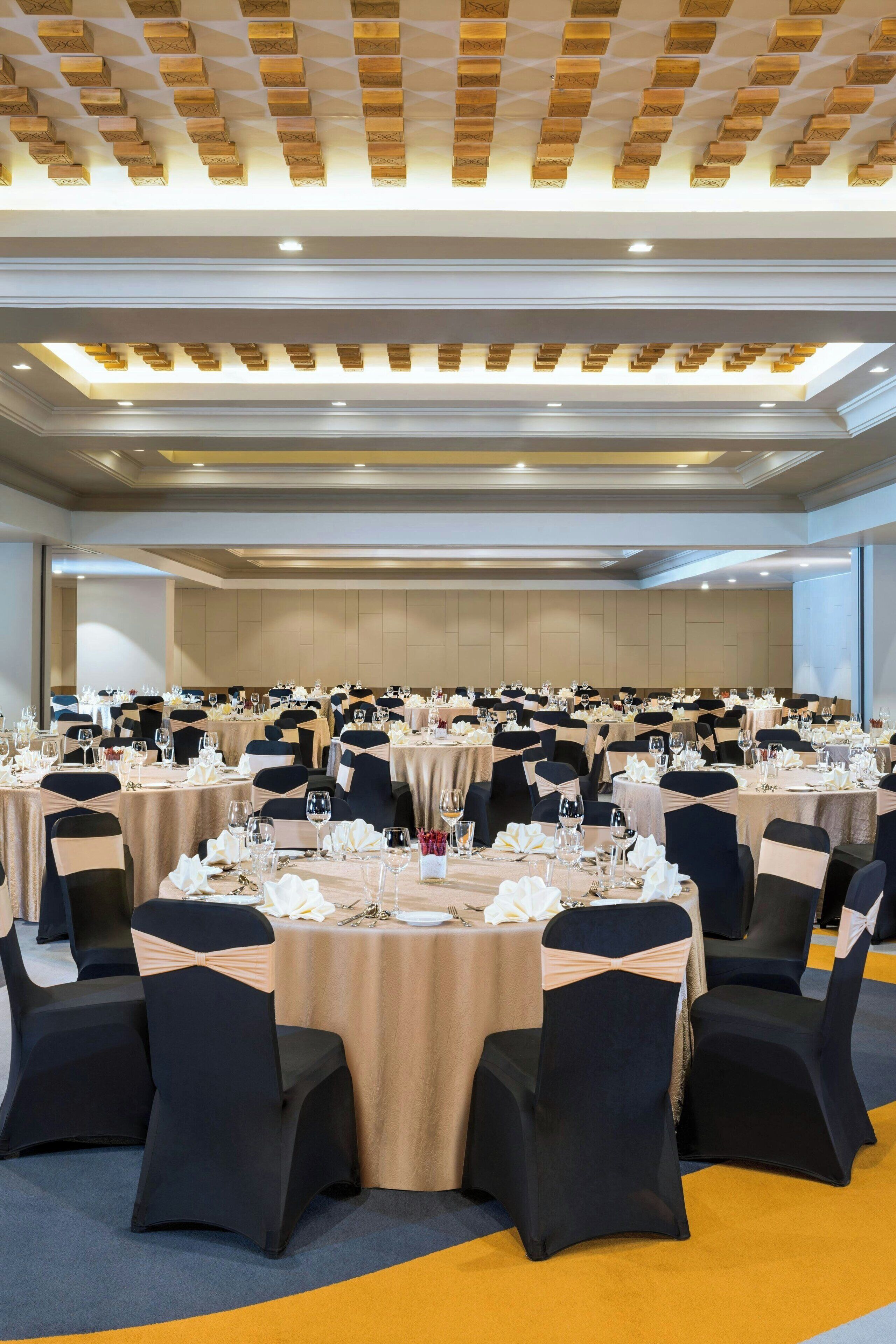 Un salón de banquetes con mesas redondas dispuestas para comer, cada una con sillas y vajilla.