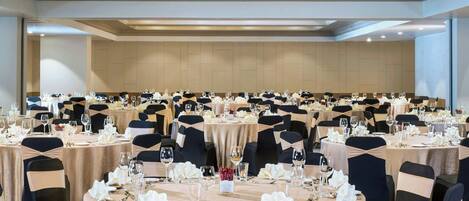 Un salón de banquetes con mesas redondas dispuestas para comer, cada una con sillas y vajilla.