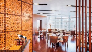 A modern restaurant with a wooden log wall, wooden furniture, and large windows offering city views.