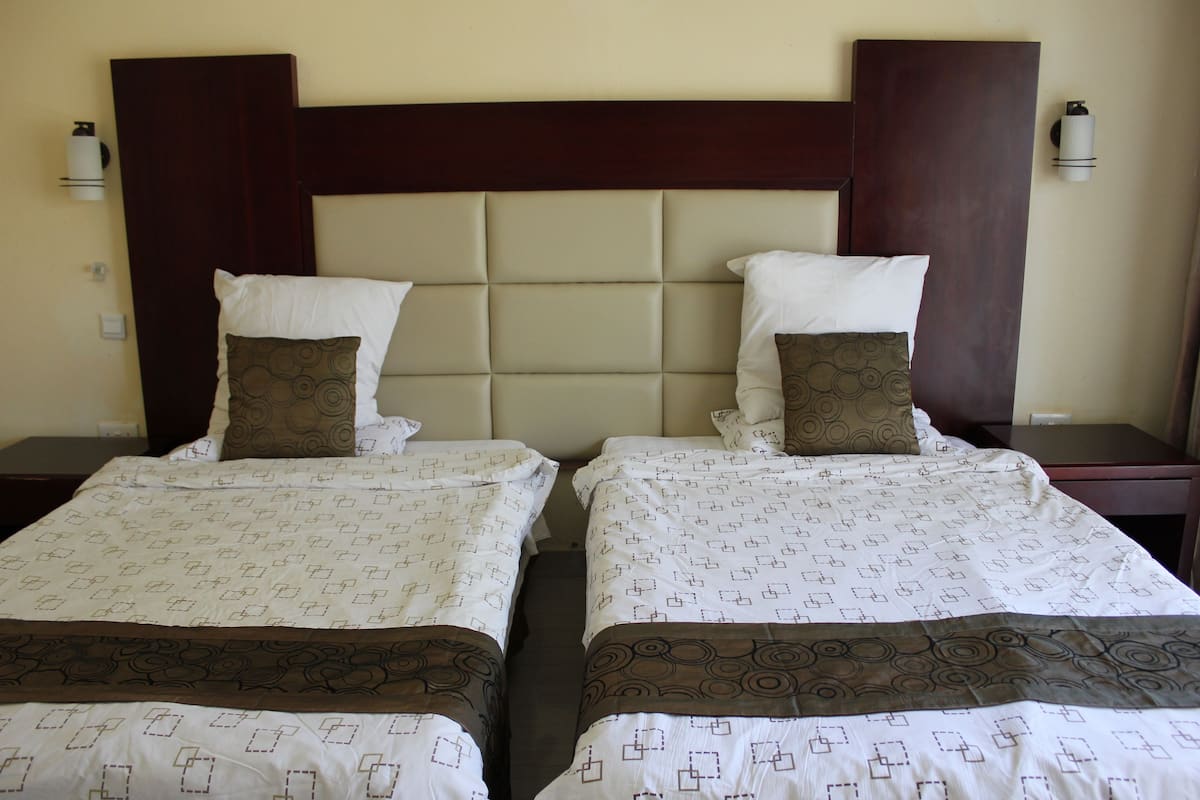 Deux lits avec des têtes de lit, du linge de lit blanc orné de motifs géométriques et une tête de lit en bois foncé.