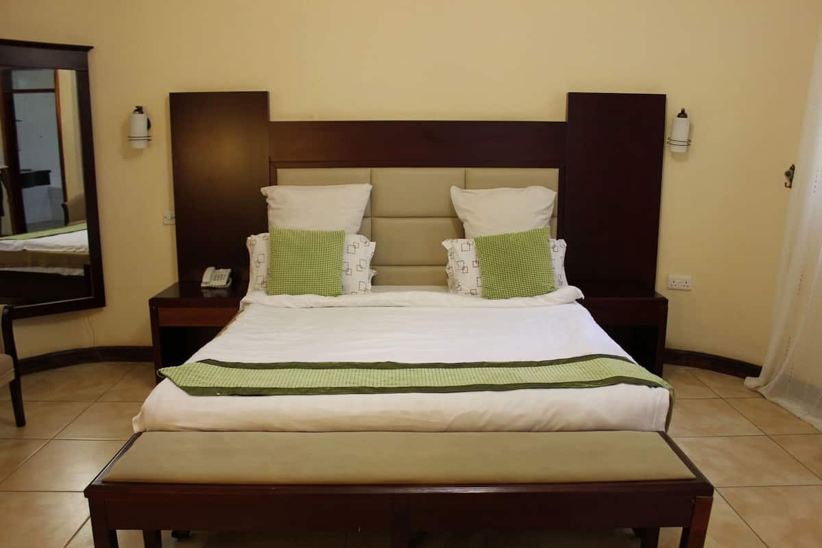 Une chambre d’hôtel avec un grand lit, deux tables de chevet, une commode, un miroir et une fenêtre.