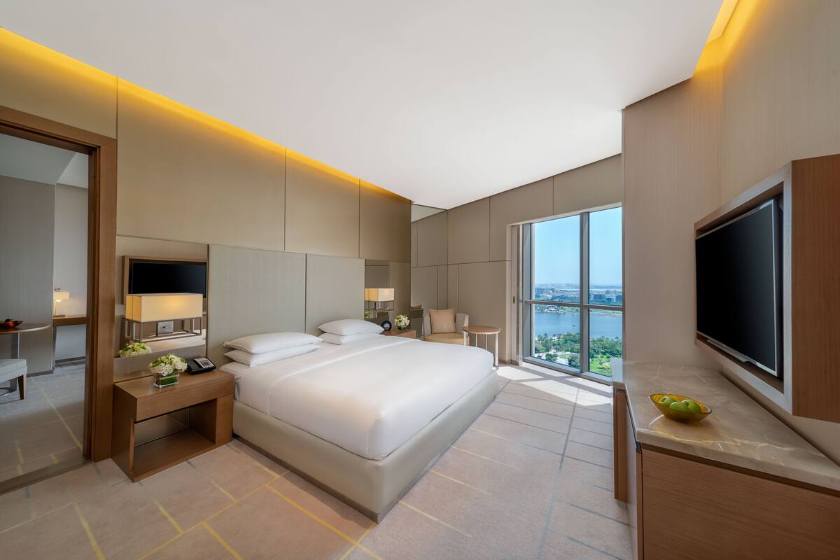 Ein modernes Hotelzimmer mit einem großen Bett, Nachttischen, einem Fernseher und Blick auf die Stadt.