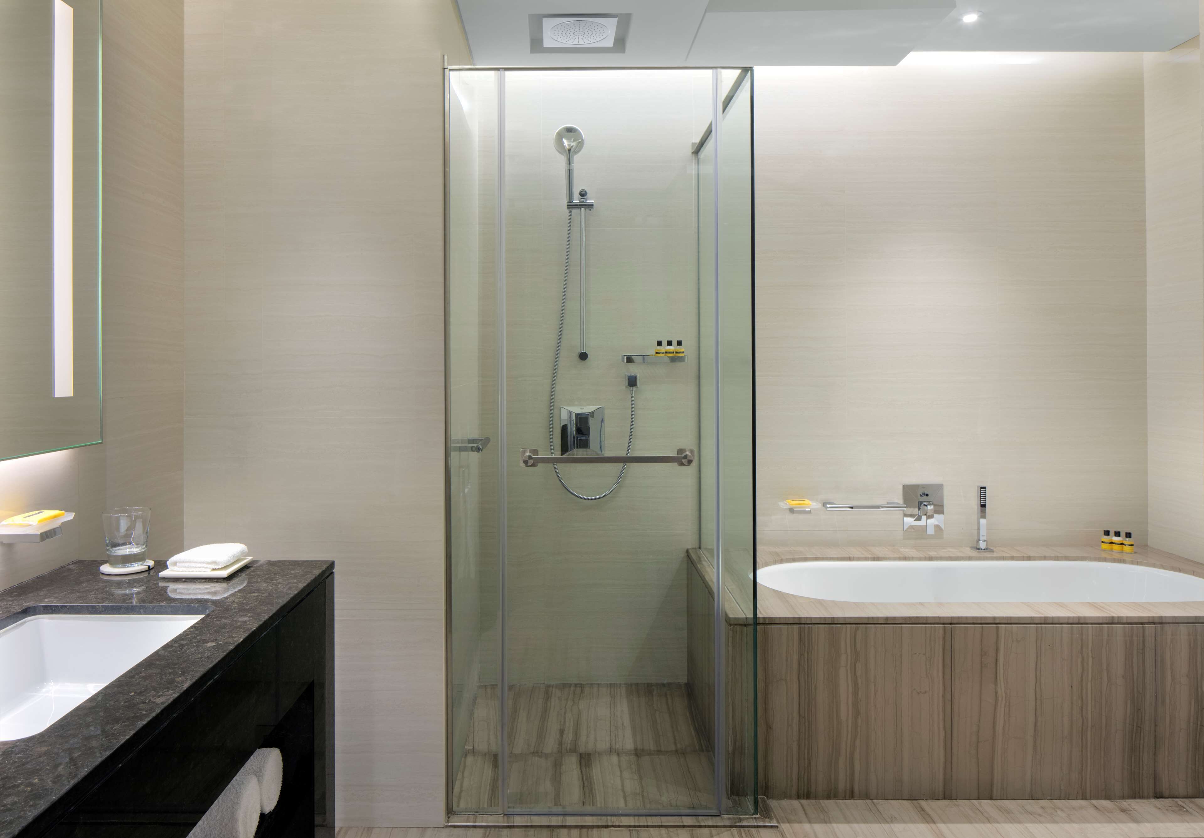 Un baño moderno con ducha de vidrio, una bañera grande y un lavamanos sobre encimera de mármol.