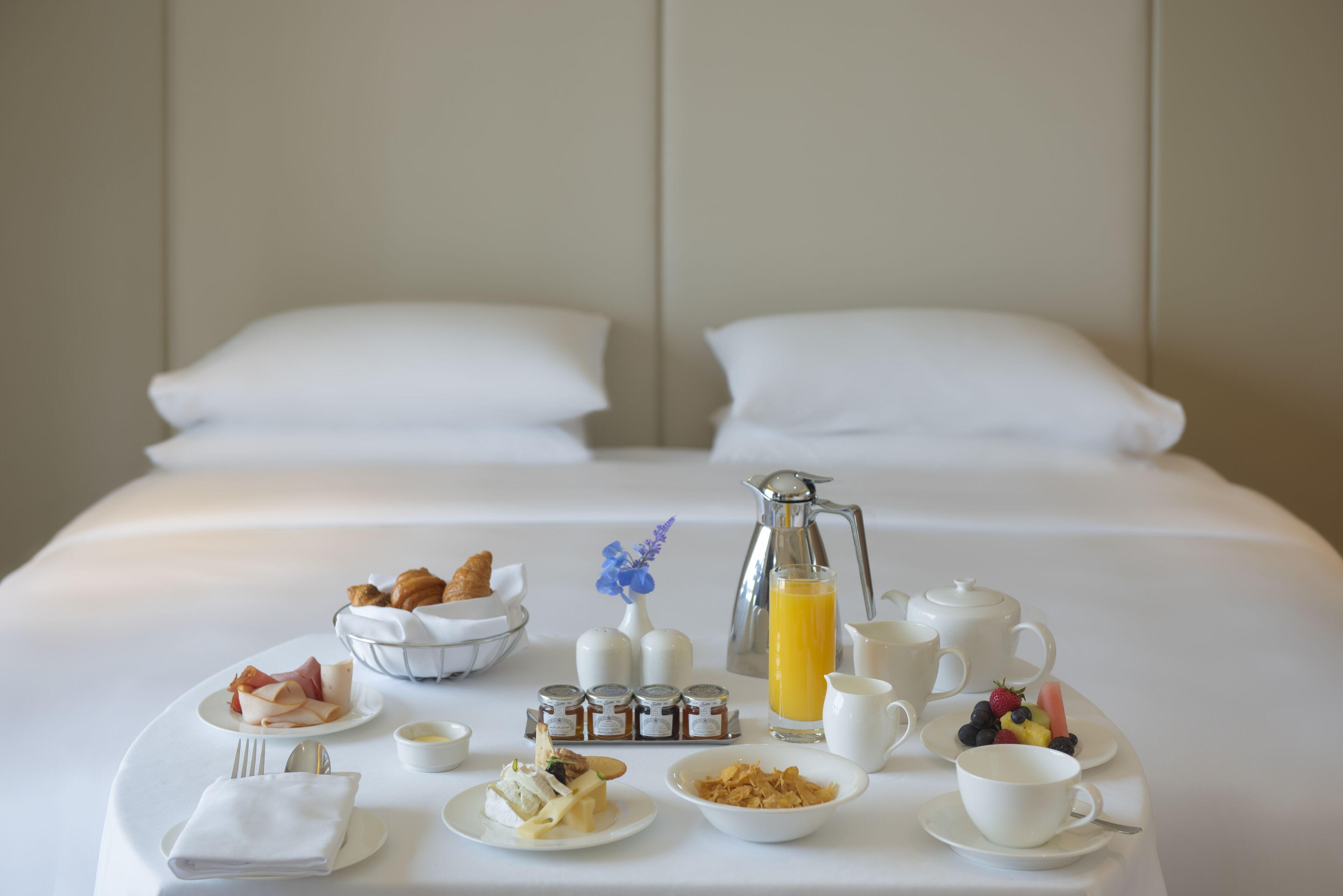 A neatly arranged breakfast buffet on a hotel bed with a variety of food items, including pastries, fruits, and beverages.