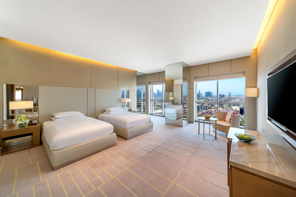 Ein modernes Hotelzimmer mit zwei Betten, einem Schreibtisch, einem Fernseher und einem großen Fenster mit Blick auf die Stadt.