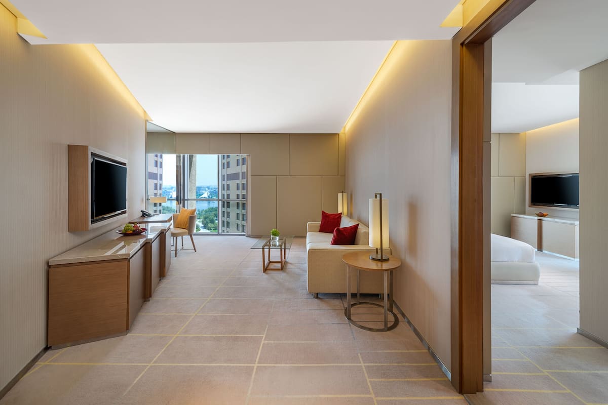 Ein modernes Hotelzimmer mit einem Flachbildfernseher, einer Couch mit roten Kissen, einem kleinen Beistelltisch und einem großen Fenster mit Blick auf die Stadt.