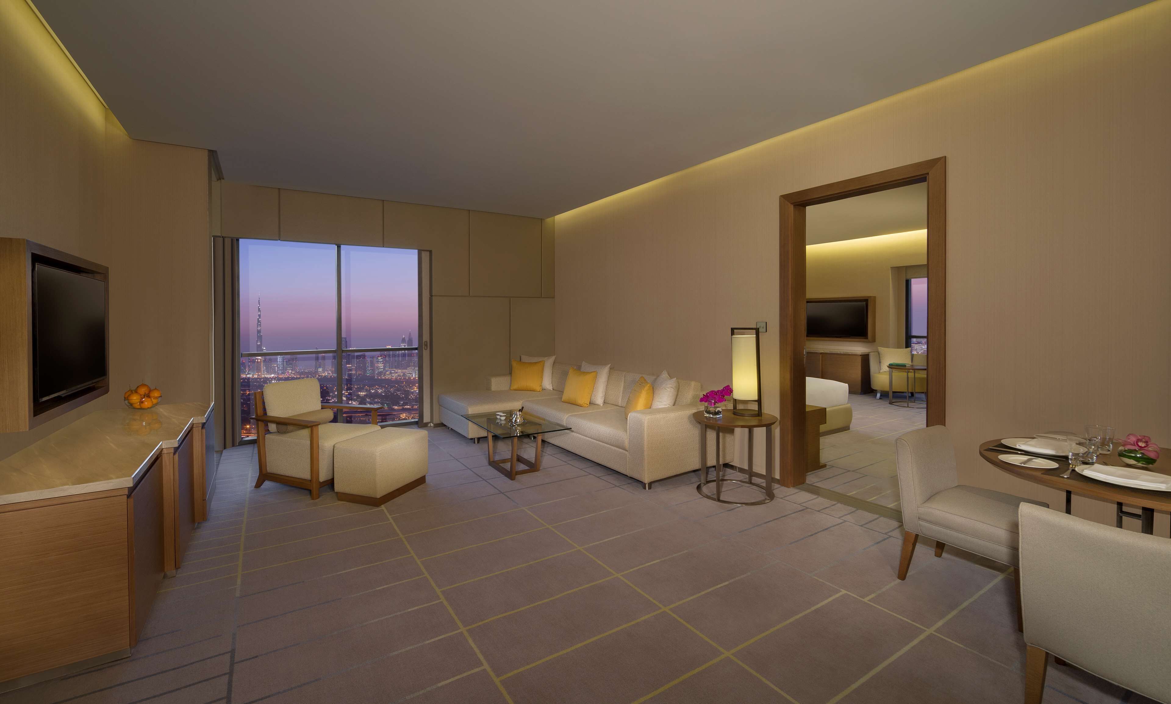 Une chambre d’hôtel moderne dotée d’une grande fenêtre donnant sur la ville, d’un canapé, d’une table basse et d’un coin repas avec un téléviseur.