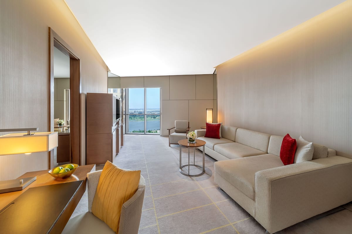 Ein modernes Hotelzimmer mit einer Sitzecke, einem kleinen Tisch mit Obstschale, einem Sessel und Blick ins Freie.