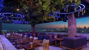 Un bar situé sur un toit, avec des places assises, une vue sur la ville et des guirlandes lumineuses.