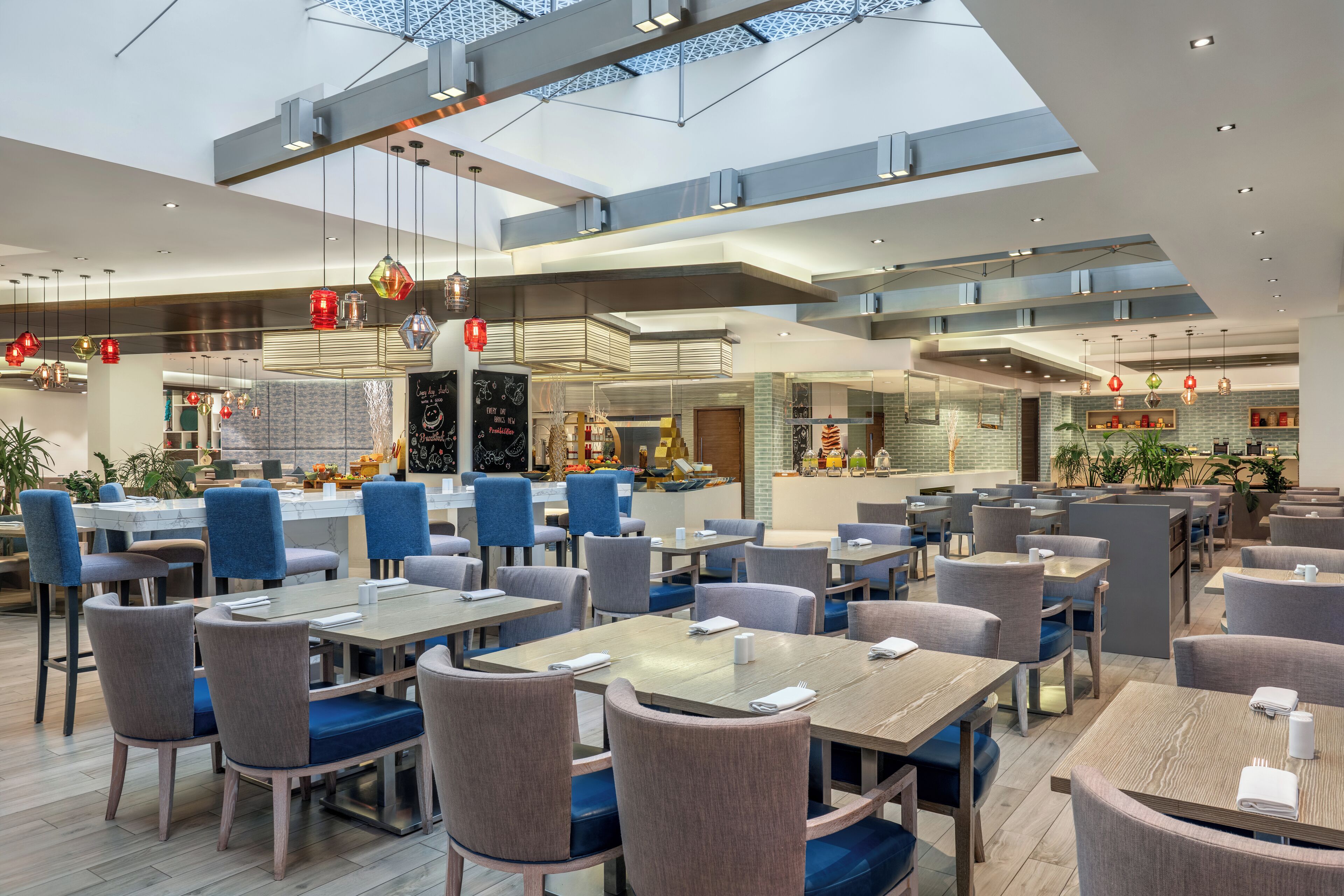A modern restaurant with multiple dining areas, high ceilings, and natural light from skylights.